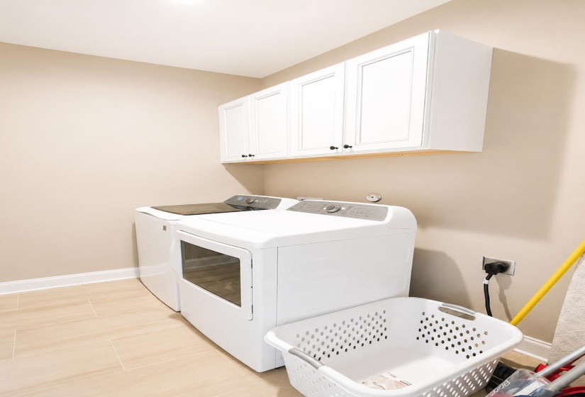 Dedicated laundry area featuring a light-toned tile floor, neutral wall paint, and white upper cabinetry with black hardware