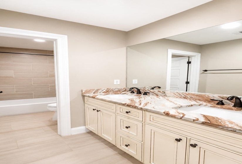 Double vanity featuring a light-colored cabinetry with dark hardware and a variegated stone countertop