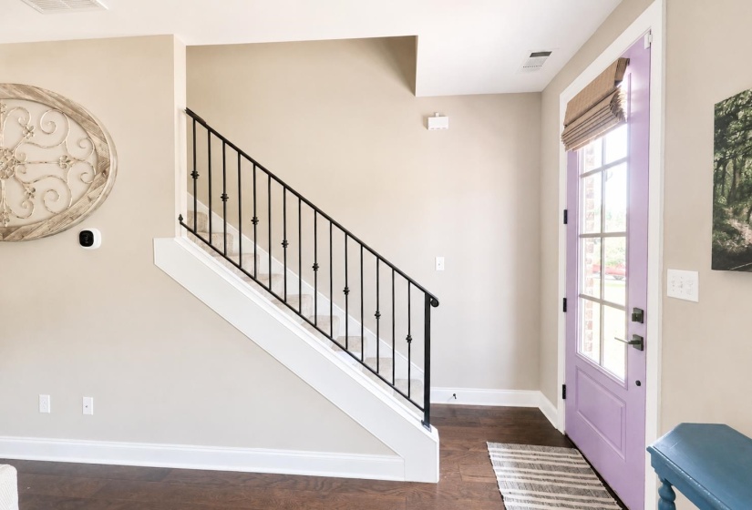 Entryway featuring a lavender glass-paneled door, dark wood-finish flooring, and a staircase with white risers and black iron balusters