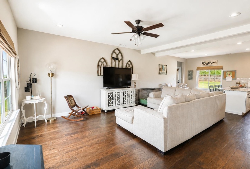 Open-concept living area with dark wood-finish flooring, vaulted ceilings with exposed beams, recessed lighting, and a ceiling fan