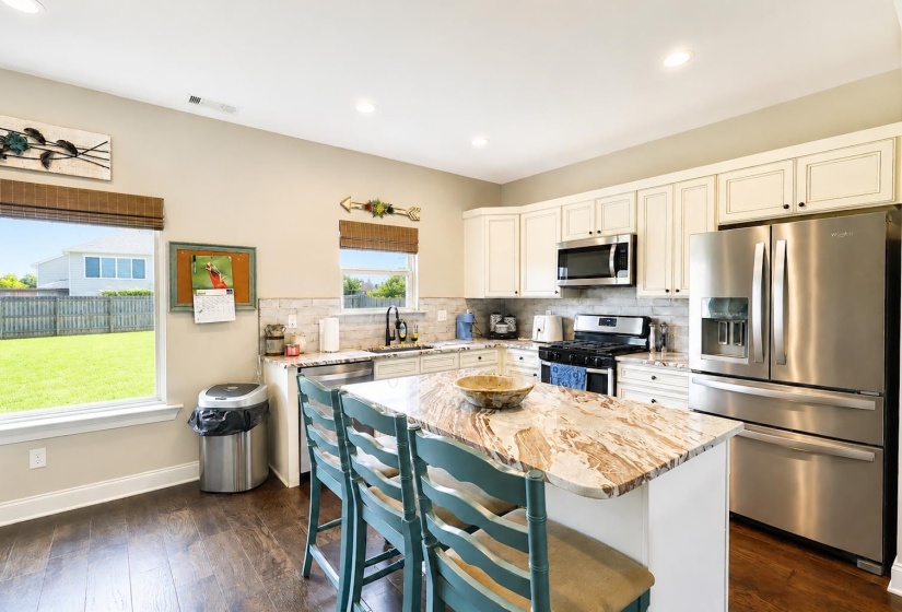Spacious kitchen with a central island featuring a granite countertop, wood-finish flooring, stainless steel appliances, and abundant cabinetry