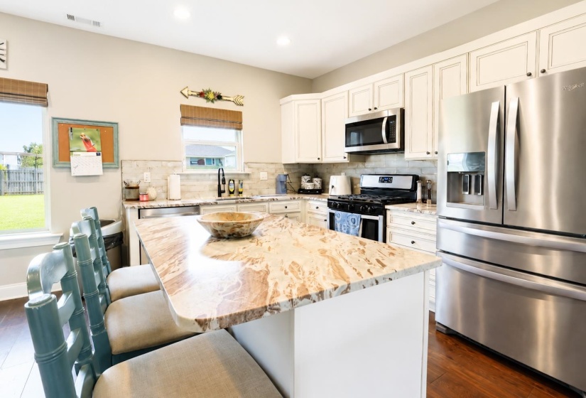 Kitchen featuring a large island with a stone countertop, white cabinetry, stainless steel appliances, and wood-finish flooring