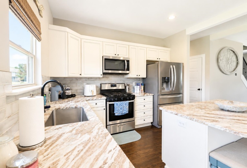 Kitchen featuring white cabinetry, stainless steel appliances, speckled countertops, and a subway tile backsplash