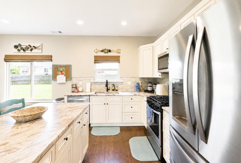 Kitchen featuring white cabinetry, wood-finish flooring, stainless steel appliances, and a central island with a light-toned countertop