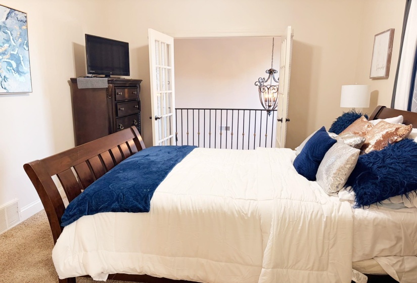 Bedroom featuring French doors opening to a wrought iron railing, a dark wood dresser, and a decorative chandelier