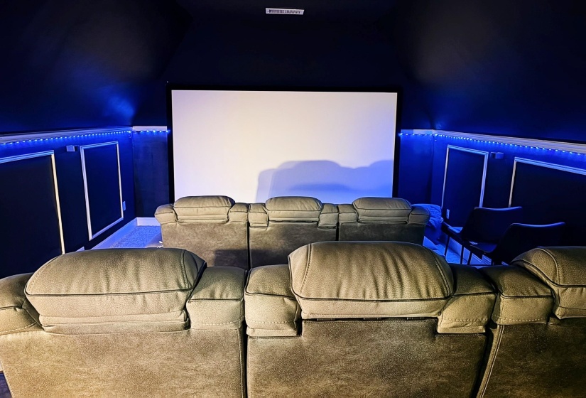 Dedicated media room featuring a large projection screen, dark wall finishes, accent lighting, and carpeted flooring