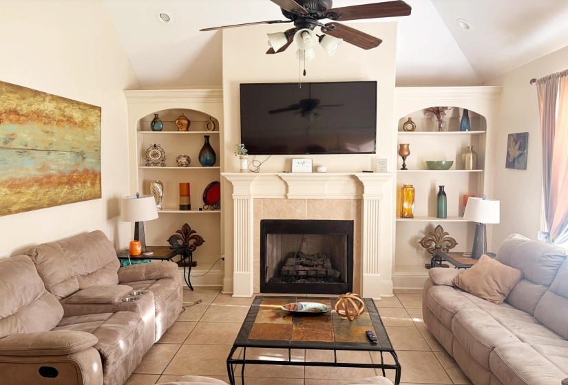Living area featuring a fireplace with a tile surround, built-in shelving, vaulted ceiling, recessed lighting, and a ceiling fan