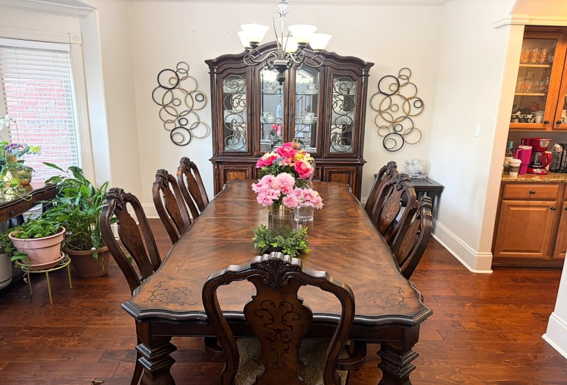 Spacious dining area featuring wood-finish flooring, a decorative chandelier, and an arched doorway leading to an adjacent space with light wood cabinetry and granite countertops