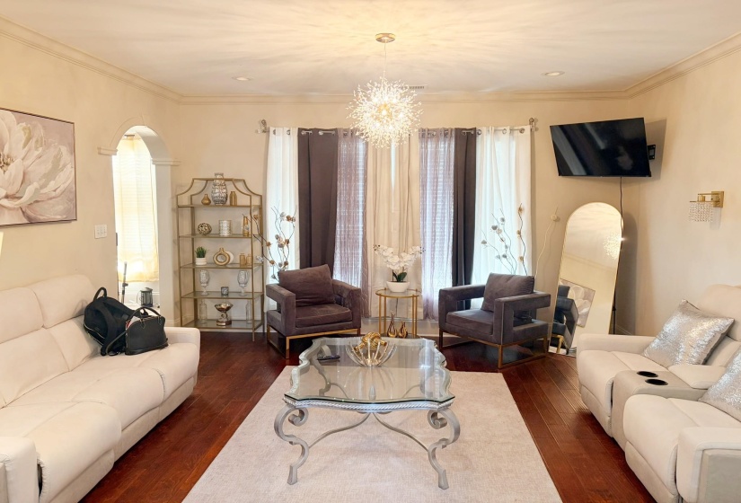 Open living area featuring wood-finish flooring, an arched doorway, crown molding, a decorative chandelier, and recessed lighting