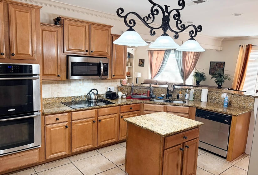 Kitchen featuring wood-finish cabinetry, granite countertops, tile flooring, stainless steel appliances including a built-in double oven, and a central island