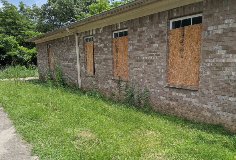 Brick exterior structure with multiple window openings, each secured with wood boarding