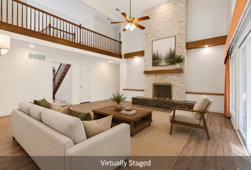 Vaulted ceiling living area featuring a floor-to-ceiling stone-clad fireplace with a wood mantle, wood-finish flooring, a second-story interior balcony with wood railing, and sliding glass doors