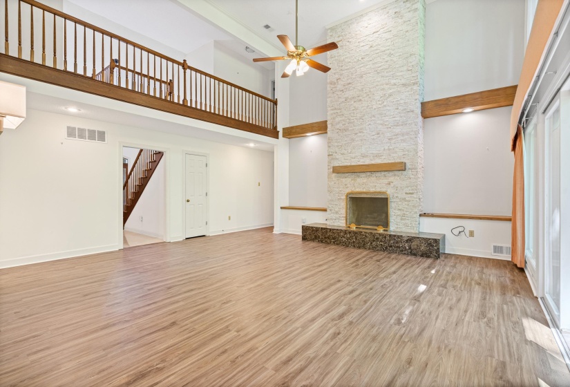 Vaulted ceiling living space featuring wood-finish flooring, a stone-clad fireplace with a dark stone hearth, a ceiling fan, and a second-story interior balcony with wood railings