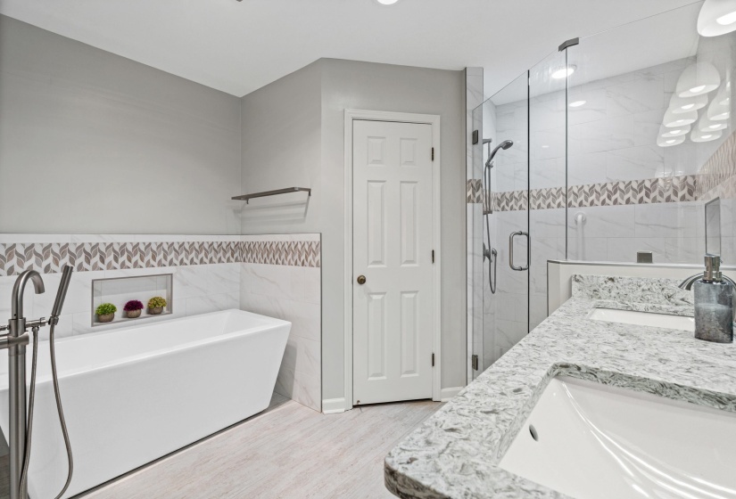 Bathroom featuring a freestanding tub with a floor-mounted faucet, an in-wall niche, a walk-in shower with a glass enclosure, and a double vanity with integrated sinks and a light-toned countertop
