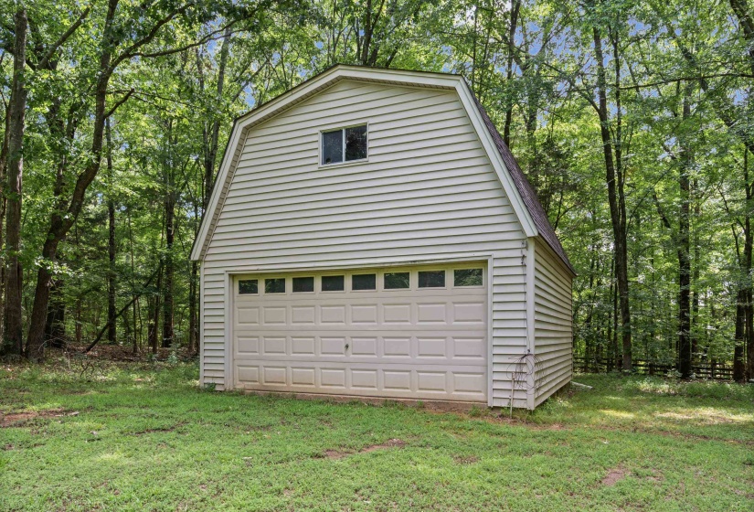 Standalone two-story structure featuring a gambrel roofline, horizontal siding, and a single vehicle garage door with upper window inserts