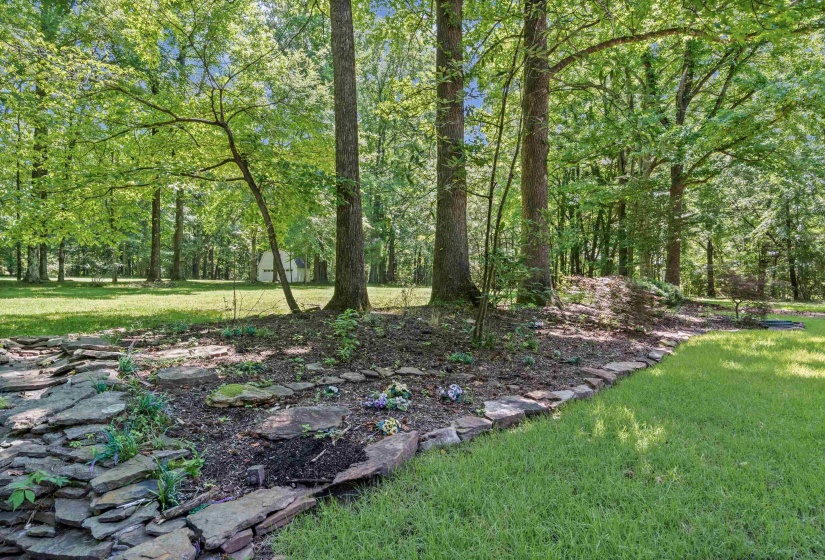 Expansive outdoor space featuring a manicured lawn, established trees, and natural stone landscaping