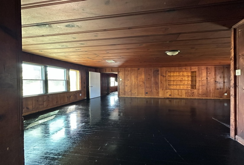 Spacious interior room featuring wood paneling, wood-finish flooring, built-in shelving, and multiple windows