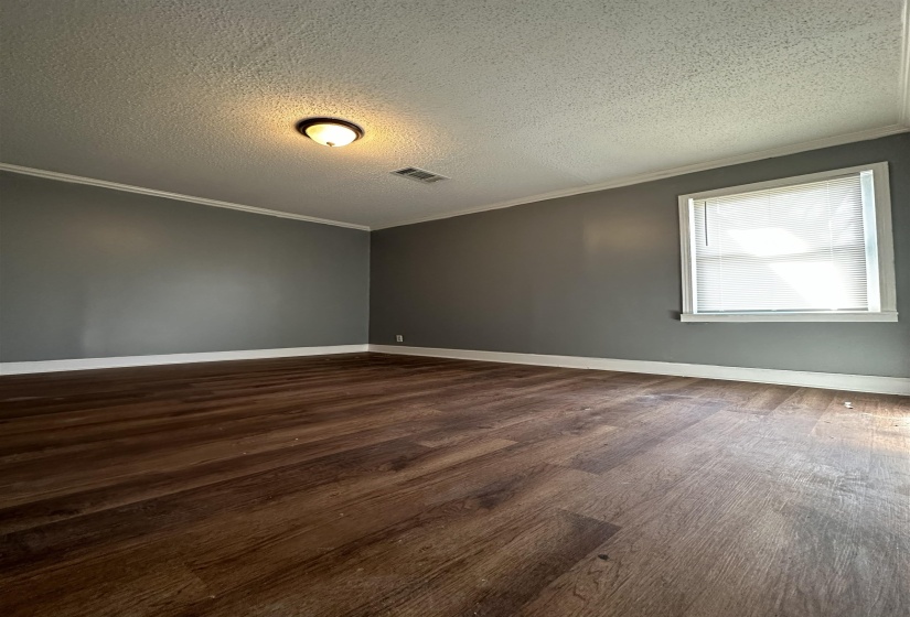 Spacious room featuring wood-finish flooring, neutral gray walls, white baseboards, and crown molding