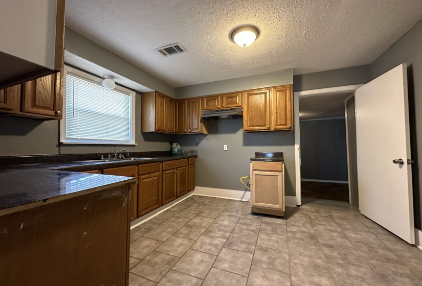 Kitchen featuring ample wood cabinetry, dark countertops, a stainless steel sink, and tile flooring