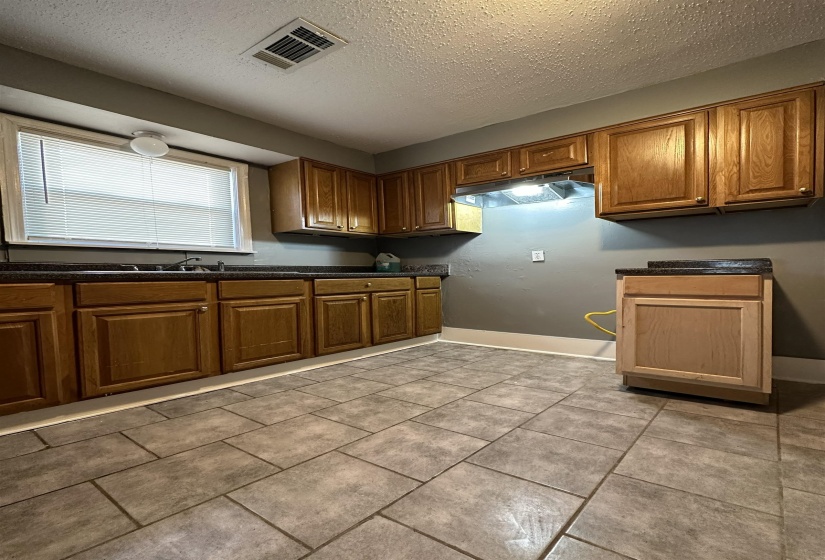 Kitchen featuring wood cabinetry with dark countertops, tiled flooring, and a window with blinds