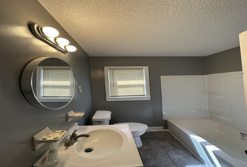 Compact bathroom featuring a white vanity with integrated sink, coordinating toilet, and a white bathtub with a shower surround