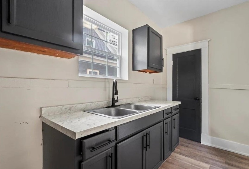 Kitchen area featuring matte black cabinetry, a double-basin stainless steel sink with a matte black faucet, and light-toned countertops