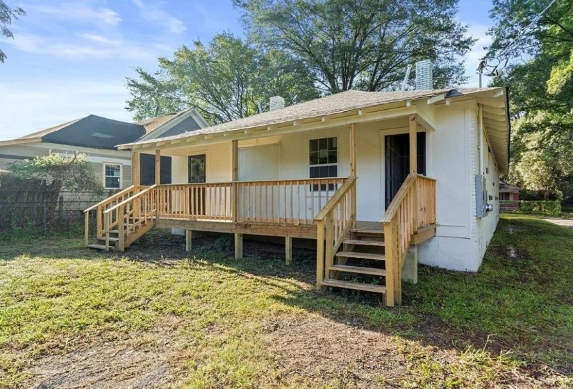 Rear exterior featuring a covered porch with natural wood railing and steps, white siding, and a gabled roofline
