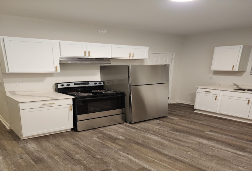 Modern kitchen featuring stainless steel appliances, white cabinetry with gold-tone hardware, white countertops, and wood-finish flooring