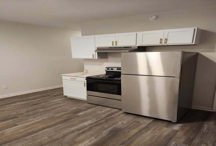Kitchen area featuring wood-finish flooring, white cabinetry with gold-toned hardware, white countertops, and stainless steel appliances including a refrigerator, range, and range hood