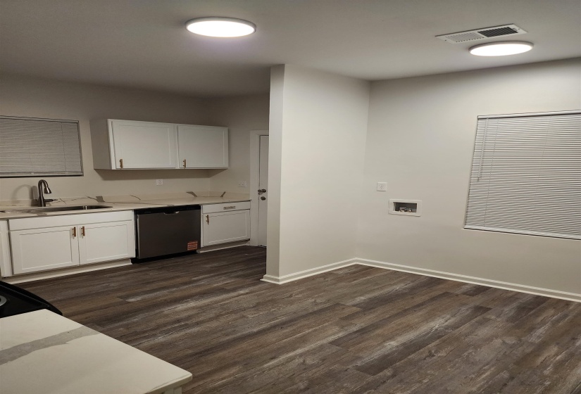 Kitchen area featuring white cabinetry with brushed bronze hardware, stainless steel dishwasher, and light-toned countertops