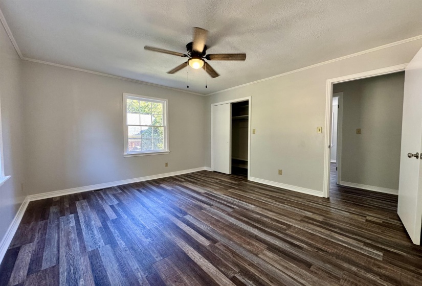 Unfurnished bedroom with ornamental molding, dark wood-type flooring, a textured ceiling, ceiling fan, and a closet