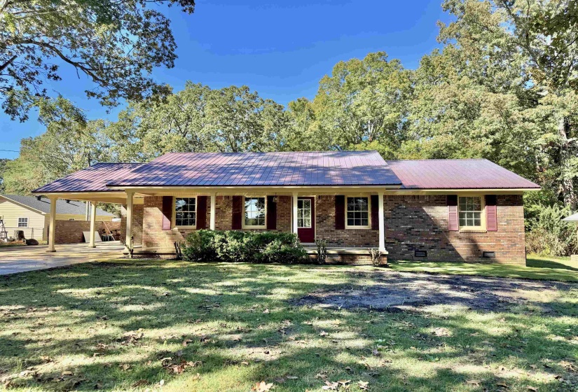 Single story home featuring a metal roof, a porch, an attached carport, and brick siding