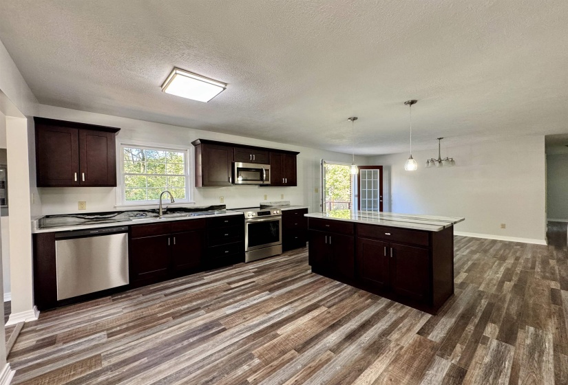 Kitchen featuring dark brown cabinetry, appliances with stainless steel finishes, hanging light fixtures, a textured ceiling, and a center island
