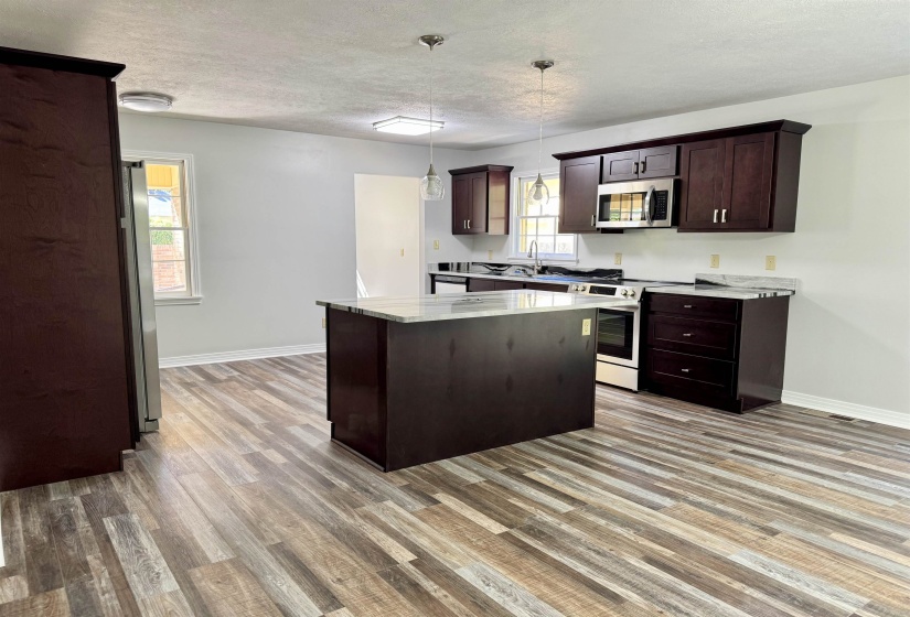 Kitchen featuring appliances with stainless steel finishes, a center island, a textured ceiling, dark brown cabinets, and pendant lighting
