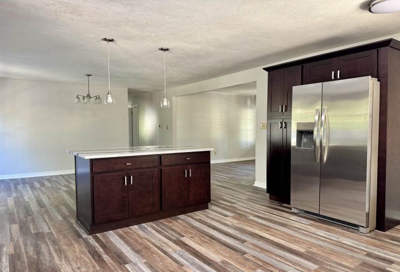 Kitchen featuring dark brown cabinetry, stainless steel fridge with ice dispenser, a textured ceiling, light wood-style flooring, and hanging light fixtures