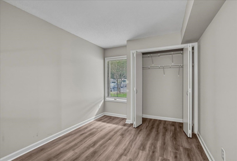 Room featuring wood-finish flooring, a window with blinds, bi-fold closet doors, and white baseboards
