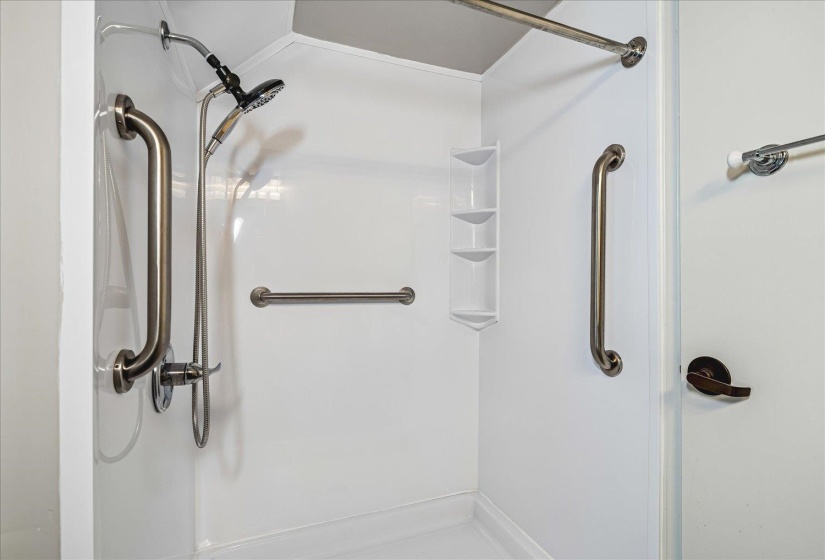 Walk-in shower with white composite surround, multiple brushed nickel grab bars, and a multi-function shower head