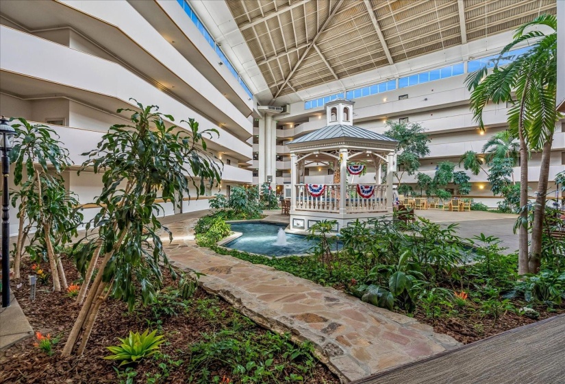 Grand atrium with a central gazebo, water feature, extensive interior landscaping, stone pathway, and multi-level balconies