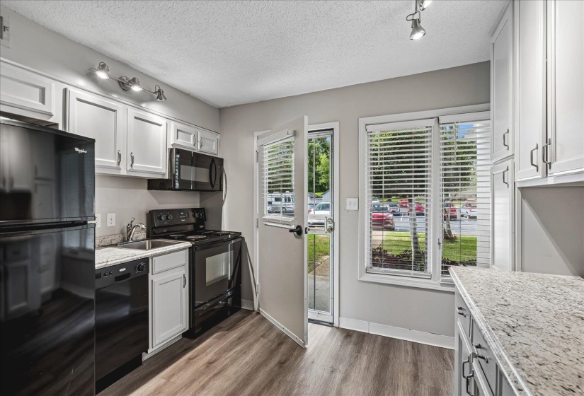Kitchen featuring wood-finish flooring, white cabinetry, dark countertops, and black appliances