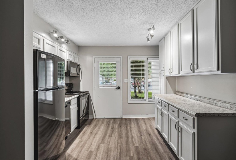 Bright kitchen featuring wood-finish flooring, white cabinetry, track lighting, and a window with horizontal blinds