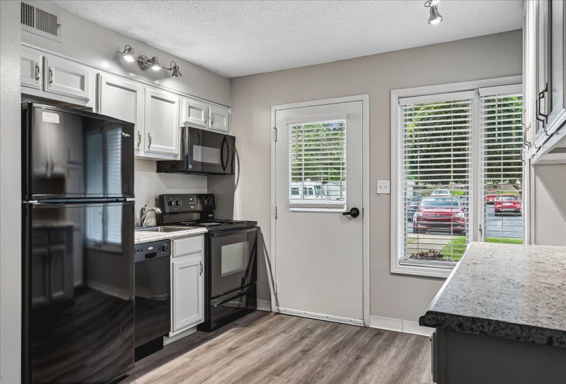 Kitchen featuring black appliances, wood-finish flooring, white cabinetry, and light-toned countertops