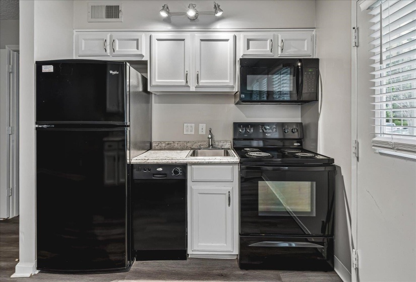 Compact kitchen featuring white cabinetry, black appliances, a granite-finish countertop, and a stainless steel sink