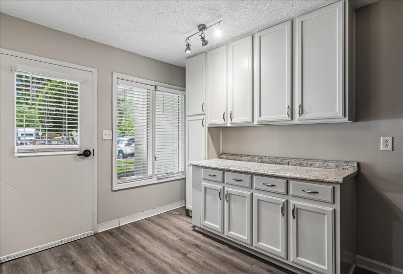 Built-in cabinetry with light-colored countertops, track lighting, wood-finish flooring, and a window with horizontal blinds
