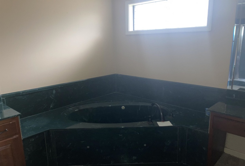 Corner soaking tub with a dark finish, surrounded by a dark stone-finish deck and half-wall