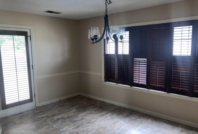 Dining area featuring dark wood plantation shutters, a multi-light chandelier, and tile flooring