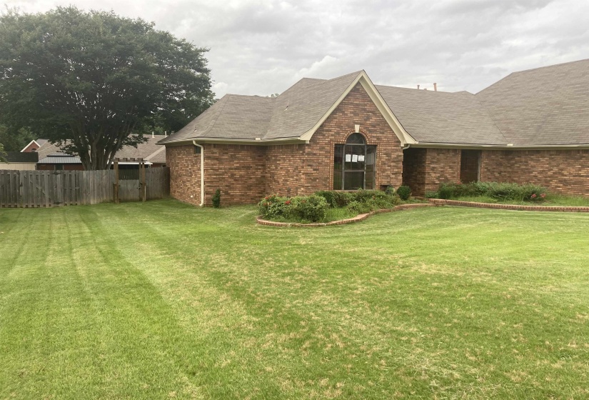 Brick exterior featuring a gabled roofline, arched window, and established landscaping
