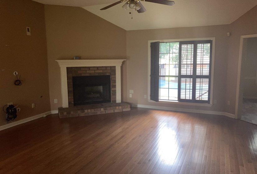Spacious living area featuring a brick fireplace with a white mantle, wood-finish flooring, and a vaulted ceiling