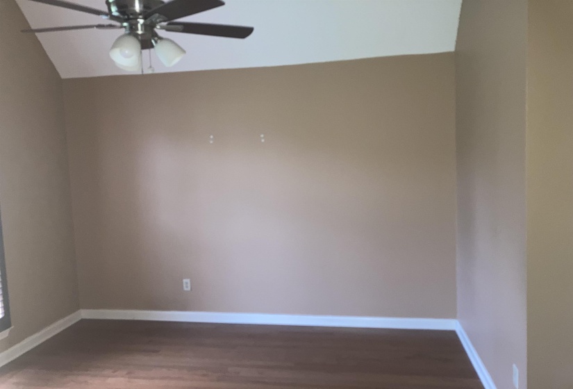 Room featuring vaulted ceilings, wood-finish flooring, neutral wall tones, and a ceiling fan with integrated lighting