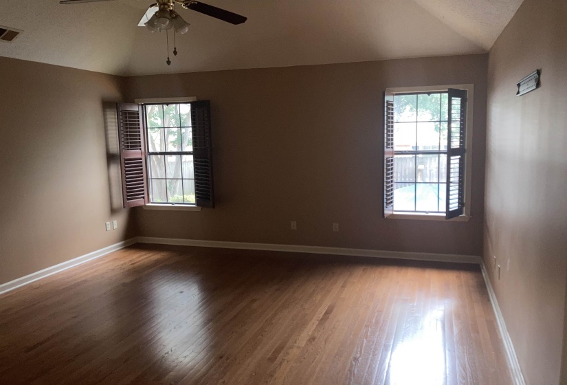 Room featuring wood-finish flooring, two windows with louvered shutters, a ceiling fan, and vaulted ceilings