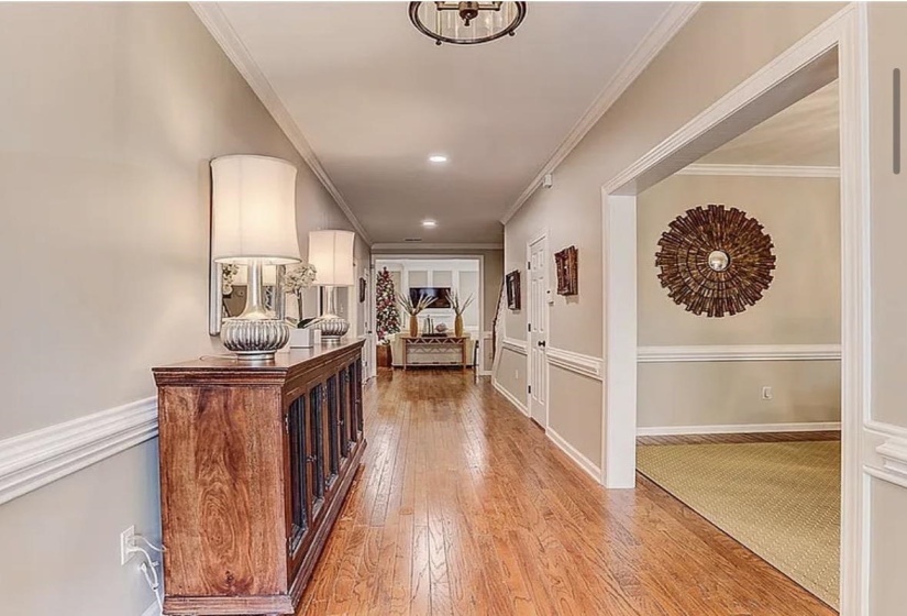 Long hallway featuring hardwood flooring, crown molding, chair rail, recessed lighting, and an open doorway to another room